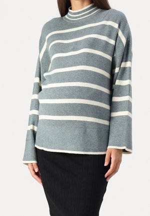 Woman wearing a gray and white horizontal striped ribbed sweater with long sleeves and a high neckline, paired with a black textured skirt.