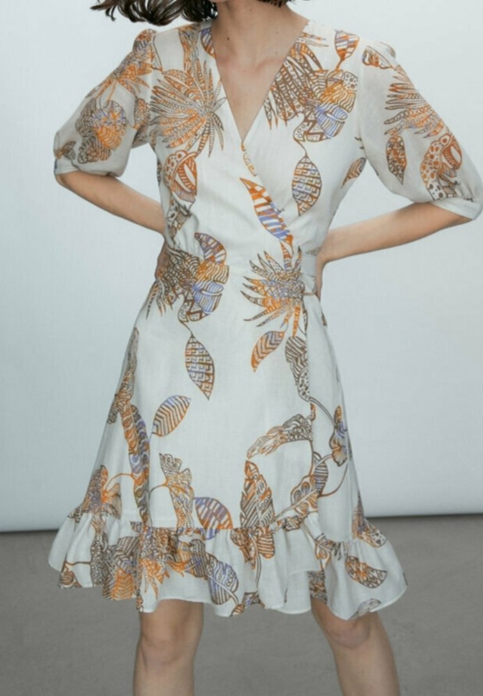 Robe portefeuille à motif floral en crème, comportant des dessins orange et bleu. Manches courtes bouffantes et ourlet à volants ajoutent texture et forme.