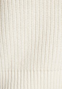 Strickstoff in cremefarbener Farbe mit einem strukturierten, gerippten Muster; weiche Textur mit leicht dickerem Bündchendetail am unteren Rand.