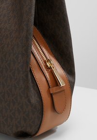Sac à main marron à motifs avec une finition en cuir lisse couleur tan, doté d'une fermeture éclair dorée et de détails sur le côté.