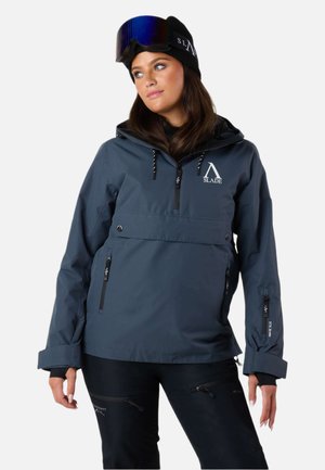 Veste imperméable gris foncé avec une poche frontale zippée, des manches réglables et des détails de logo ; portée avec un pantalon noir et un bonnet.