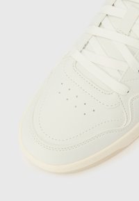 Prikaz izbliza prednjeg dijela bijele tenisice s bijelim vezicama i rupicama za ventilaciju na području prsta.