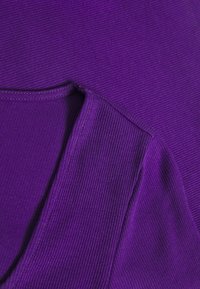 Lila gerippter Stoff mit einem runden Ausschnitt und sichtbaren Nähdetails. Die Textur ist weich mit einem gleichmäßigen, einheitlichen Muster.