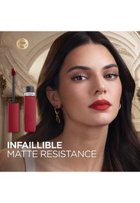 Rouge à lèvres liquide avec finition mate dans un tube rectangulaire élégant. Le modèle porte un rouge à lèvres audacieux, présenté avec des boucles d'oreilles en métal doré.