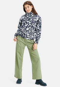 Fleece pullover met een marineblauw bloemenpatroon op een lichte achtergrond, met een halve rits kraag; gecombineerd met olijfgroene wijde benen broek en marineblauwe enkellaarsjes.