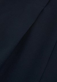 Tumši zils audums ar gludu tekstūru, tam ir asas locījumi un strukturēts dizains. Minimālas detaļas, uzsvars uz tīrām līnijām.