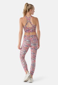 Conjunto de sujetador deportivo y leggings coloridos en una tela estampada. Presenta un diseño de espalda nadadora, material elástico y ajuste hasta los tobillos.