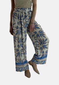 Losse, gemusterde broeken in crème met blauwe en bruine bloemenpatronen. Voorzien van een elastische tailleband en wijde pijpen.
