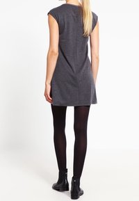 Robe grise à manches courtes, de coupe droite, en tissu texturé, avec une couture au dos. Portée avec des collants noirs et des bottines.