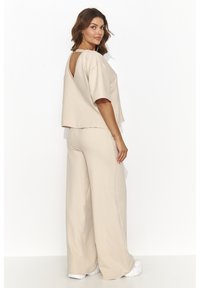 Beżowy dwuczęściowy zestaw składający się z krótkiej bluzki z wycięciem na plecach oraz luźnych spodni o szerokich nogawkach, wykonany z miękkiego materiału.