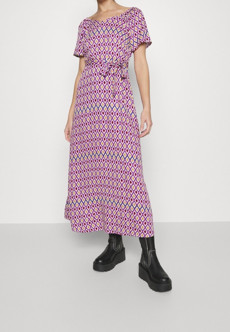 Lilla midi kjole med et diamantgeometrisk mønster i pink, gul og blå. Korte ærmer, talje bånd og letvægtsstof. Sorte platformstøvler.