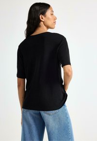Zwarte, kortärmelige t-shirt met een relaxte pasvorm en ronde halslijn, gecombineerd met lichtblauwe, losse jeans. Minimalistisch ontwerp.