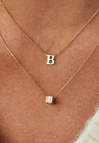 Gouden lagenkettingen met een soepele ronde hanger met een "B" en een kubus hanger met een gegraveerde "B," met delicate kettingen.