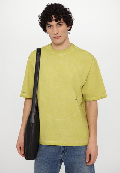 Lime green short-sleeve T-shirt with circular stitching patterns. Paired with a black textured shoulder bag. Simple design, relaxed fit.