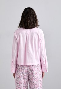 Pink cotton shirt with a straight cut and side slits, featuring a classic collar and buttoned cuffs, paired with floral-patterned pants.