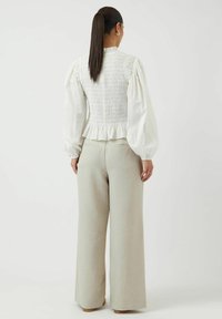 Blouse blanche smockée avec des manches bouffantes, ourlet volanté, associée à un pantalon large beige clair. Le tissu est texturé et léger.