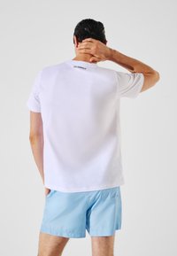 T-shirt en coton blanc avec un col rond et des manches courtes ; présente un logo noir au dos ; associé à un short bleu clair.