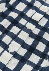 Námořnická a bílá kostkovaná košile, která má zapínání na knoflíky s kulatými bílými knoflíky a strukturovanou tkaninou. Vzor je jednotný, s výraznými čtverci.