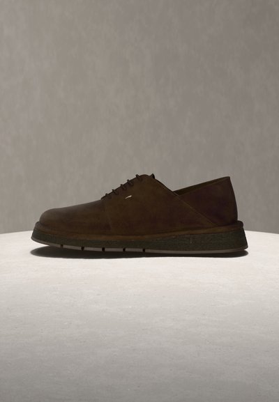 Σκούρο καφέ σουέντ κορδονωτό παπούτσι με χοντρή μαύρη σόλα, εμφανιζόμενο από το πλάι σε ανοιχτή επιφάνεια με μονόχρωμο φόντο.