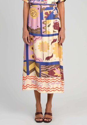 Femme portant une jupe midi colorée avec des motifs floraux et géométriques abstraits en tons jaunes, violets, bleus et rouges, assortie à des sandales marron.