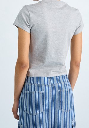 Osoba ubrana w jasnoszary krótki rękaw i niebiesko-białe spodnie w pionowe paski, pokazana od tyłu na jednolitym tle.