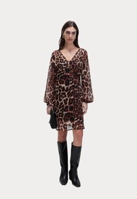 Robe en imprimé léopard transparente avec de longues manches bouffantes, décolleté en V profond et longueur mi-cuisse, associée à des bottes noires jusqu'aux genoux et un petit sac noir.