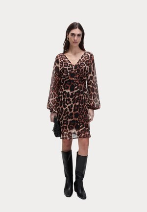 Robe en imprimé léopard transparente avec de longues manches bouffantes, décolleté en V profond et longueur mi-cuisse, associée à des bottes noires jusqu'aux genoux et un petit sac noir.