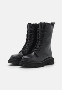 Bottines en cuir noir avec un laçage à l'avant, doublure en fourrure et semelles épaisses. Elles présentent une texture lisse et un design à bout rond.
