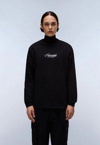 Juoda ilgomis rankovėmis golfas iš minkšto audinio, krūtinės srityje su baltais užrašo raidėmis. Paprastas dizainas su klasikinio kirpimo siluetu.