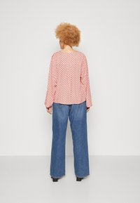 Red and white patterned long-sleeve top, paired with loose blue denim jeans, featuring a straight cut, visible seams, and black footwear.