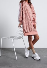 Růžové oversized šaty s leopardím potiskem a bílými třemi pruhy na rukávech. Dokončeno s bílými teniskami a béžovými ponožkami.