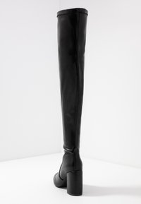 Bota negra de muslo alto hecha de cuero suave con tacón bloque, que presenta un diseño sin costuras y costuras sutiles a lo largo de la parte posterior.