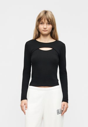 Noor naine sirgete blondide juustega, kes kannab musta pika varrukaga tippi rinnalõikega ja valgeid dressipükse, millel on "GAP" logo.