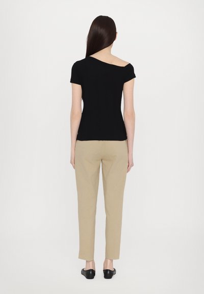Top negru cu umeri descoperiți și mâneci scurte, asortat cu pantaloni bej tapered și pantofi slip-on negri, văzut din spate.
