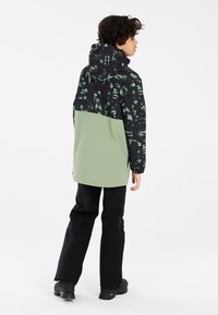 Giacca nera e verde con la parte superiore a decori, parte inferiore verde olivastro uniforme, abbinata a pantaloni neri e calzature nere robuste.