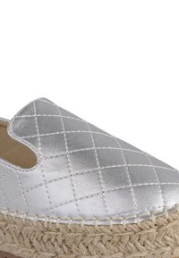 Scarpa slip-on argento trapuntata con suola in giuta espadrille e dettagli intrecciati. Texture liscia con cuciture a contrasto e bordo intrecciato.