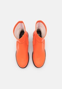 Botas de tobillo impermeables en color naranja con un acabado suave, punta redondeada y un pequeño tacón. El interior cuenta con un forro de color claro y una plantilla texturizada.