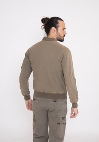 Chaqueta bomber de color verde oliva con puños y dobladillo acanalados, que presenta una tela texturizada y bolsillos laterales, combinada con pantalones cargo a juego.