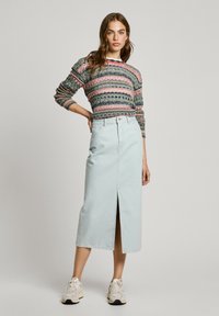 Strikket genser med flerfargede horisontale striper, sammen med et lyseblått denimskjørt med en frontspalte. Hvite sneakers fullfører antrekket.