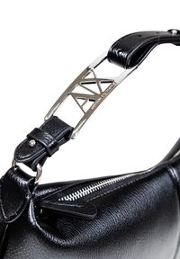 Bolso de mano de cuero negro con un conector de correa de hardware plateado que presenta las letras "AX." Superficie texturizada, cierre de cremallera y diseño elegante.