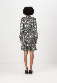 Robe à imprimé floral noir et blanc avec des manches longues, un ourlet volanté et une taille nouée. Portée avec des sandales à talons noires.