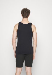 Schwarzes Tanktop mit klassischem Schnitt und glatter Textur, kombiniert mit schwarzen Shorts, von hinten vor einem weißen Hintergrund gezeigt.