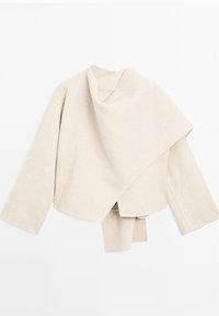 Haut enveloppant beige clair en tissu doux. Présente un design ample et drapé avec des manches larges et un ourlet asymétrique.