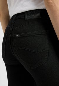 Črne jeans kratke hlače iz denima z teksturirano površino, vidnimi šivi in usnjeno oznako z napisom "Lee" na pasu ter majhnim logotipom na žepu.