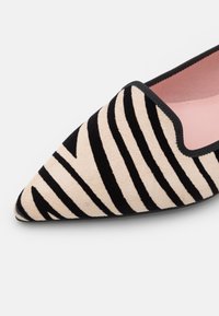 Chaussure plate pointue avec des rayures zébrées noires et beiges et une bordure noire autour de l'ouverture, montrant une doublure intérieure rose.