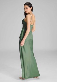 Vihreä satiininen iltapuku, jossa on vartalonmyötäinen yläosa, avonainen selkä ja ohuet olkaimet. Pitkä helma laskeutuu pehmeästi lattiaan.