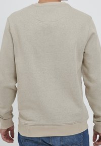 Béžová bavlněná mikina s dlouhými rukávy, žebrovanými manžetami a lemem. Hladká textura s kulatým výstřihem a minimálními švy na zadní straně.