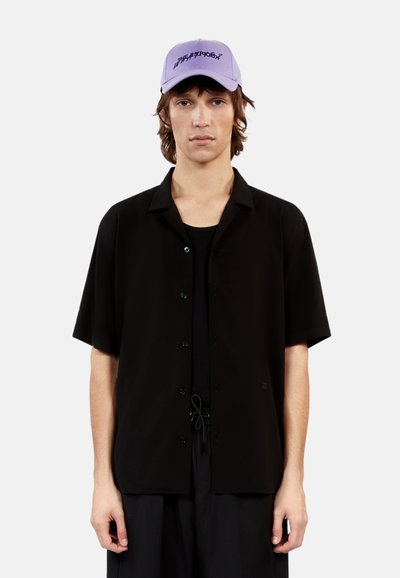 Zwarte korte mouw knoopshirt met een ontspannen pasvorm, gecombineerd met een lichtpaarse pet met donkere geborduurde tekst. Eenvoudig, modern ontwerp.