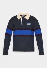 Tamsiai mėlynos vilnos mišinio polo marškiniai su kreminės spalvos apykakle, kurie turi horizontalius raštus mėlyna ir bordo spalvomis, ir mažą logotipą kairėje pusėje.