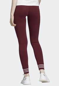 Marinröda leggings med en tight passform, slät textur och vit randaccent vid vristen. Bärs med vita sportskor.